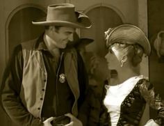 a man and woman dressed in old western clothing talking to each other while standing next to each other