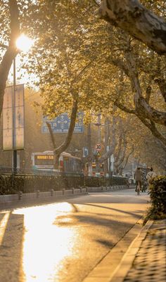 the sun shines brightly through trees on a city street as people walk down the sidewalk