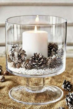 a candle that is sitting inside of a glass bowl filled with pine cones and snow