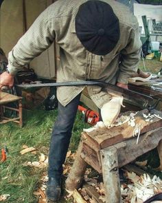 a man is working with wood in his yard while holding a large knife and looking at something