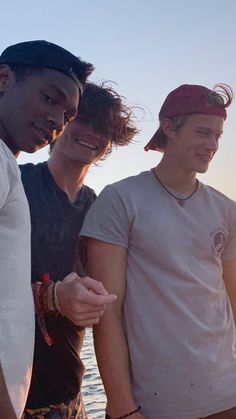 three young men standing next to each other near the ocean