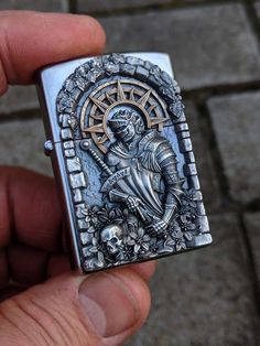 a hand holding a silver colored lighter with an image of a skeleton in the center