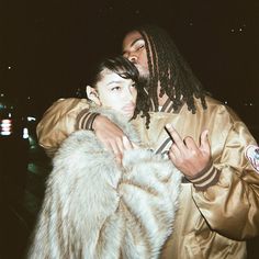 a man with dreadlocks hugging a woman in a gold jacket and fur coat