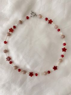 a red and white beaded bracelet with star charms on the clasp is laying on a white sheet