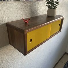 a wooden shelf with yellow drawers and a potted plant sitting on top of it