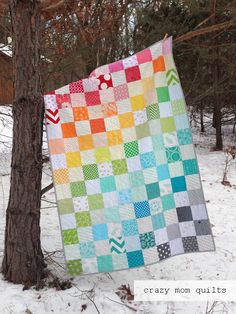 a colorful quilt hanging from a tree in the snow