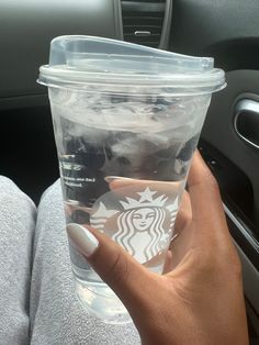 a woman holding up a starbucks cup in her hand while sitting in the backseat of a car