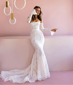 a woman in a white dress standing next to a pink wall and chandelier