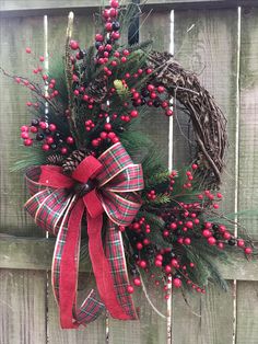 a christmas wreath hanging on the side of a wooden fence with red berries and pine cones