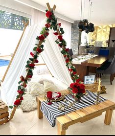 a table set up for a party with red roses and greenery on the top