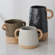 three ceramic mugs sitting next to each other on a white counter top, one with two handles