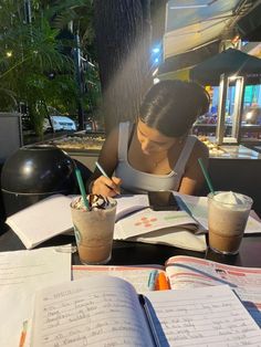 a woman sitting at a table in front of an open book and writing on paper