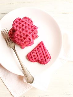 two heart shaped waffles on a white plate with a fork and napkin next to them