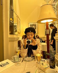 a woman sitting at a table taking a photo with her camera and wine glasses in front of her