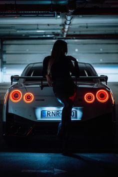 a woman standing next to a white sports car in a parking garage with the lights on