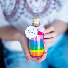 a person holding a small bottle with a name tag on it and a rainbow colored liquid inside