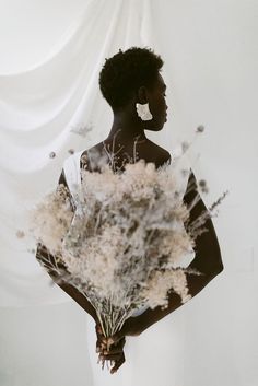 a woman holding a bouquet of flowers in front of a white curtain with her back to the camera