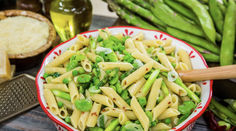 a bowl filled with pasta and peas on top of a table next to green beans