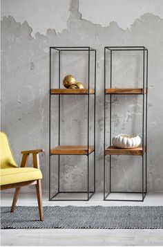 two metal shelves with wooden shelves in front of a gray wall and yellow chair next to them