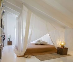 a bed with white drapes on top of it in a room filled with bookshelves