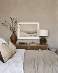 a bed with white sheets and pillows in a bedroom next to a painting on the wall