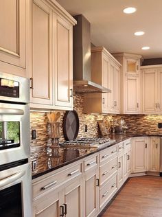 a large kitchen with white cabinets and wood flooring, along with stainless steel appliances