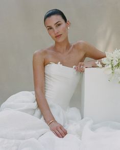 a woman in a white dress is sitting on a bed with her hand on the pillow