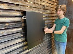 a young man standing in front of a wooden wall holding a piece of art on it