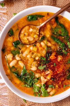 a white bowl filled with beans and spinach next to a spoon on top of a table