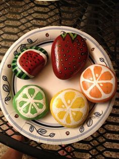 four painted rocks on a plate with strawberries and oranges