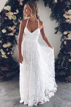 a woman standing in front of a floral arch wearing a white dress with spaghetti straps