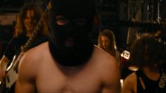 a shirtless man wearing a black mask and holding a guitar in front of other people