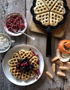 two waffles with berries and orange slices on a plate next to other food