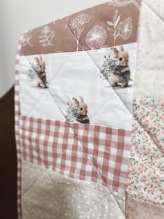 a close up of a patchwork quilt with rabbits on it's side and flowers in the background