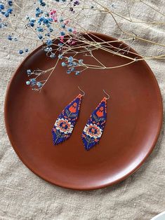 a pair of beaded earrings sitting on top of a brown plate next to flowers