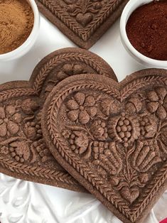 three heart shaped cookies sitting on top of a table next to two bowls of spices