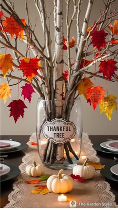 a vase filled with branches and leaves on top of a table covered in fall leaves