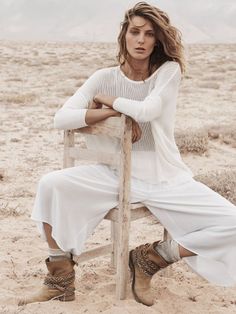 a woman sitting on top of a wooden chair in the middle of a dirt field