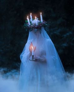 a woman wearing a veil and holding a candle in her hand with fog around her