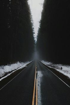 an empty road with trees and snow on the sides, in front of a dark background