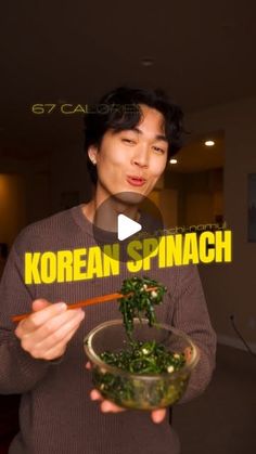 a man holding a bowl filled with greens and chopsticks in front of him