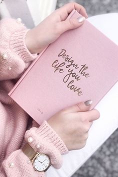 a woman holding a pink book with writing on it