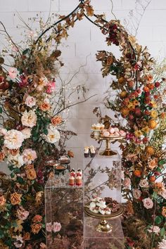 an assortment of desserts on display in front of a floral arch with candles and flowers