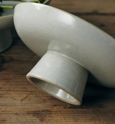 two white bowls sitting next to each other on top of a wooden table with plants in the background