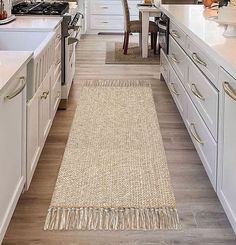 a kitchen with white cabinets and an area rug on the floor in front of the stove