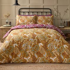 a bed covered in a yellow and pink comforter next to a night stand with a lamp on it