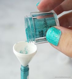 a person is holding a blue and green nail polish in their left hand, next to a small white cup with glitter on it