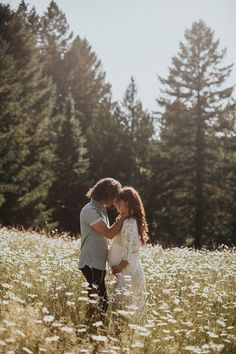 a bride and groom standing in the middle of a field surrounded by tall pine trees