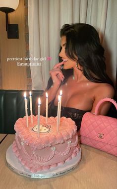 a woman sitting in front of a pink cake with lit candles