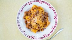 a white plate topped with pasta and meat covered in sauce on top of a table